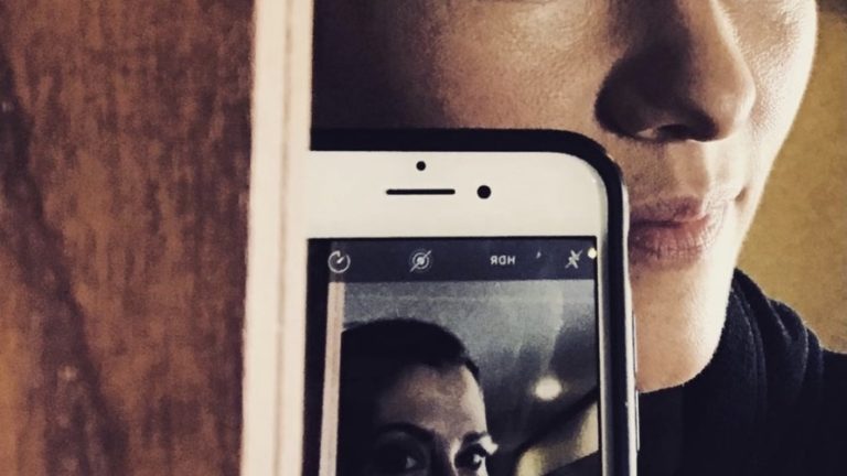 Reflection of Chyler looking in the mirror with same image on her mobile phone